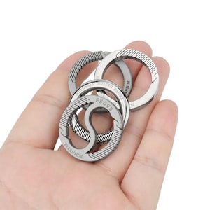 Può includere: Un set di tre anelli in titanio intrecciati con le parole "Titanium", "PBGV8", "BEAR DESIGN" e "MONON" incise su di essi.