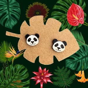 May include: A pair of wooden panda bear earrings on a brown leaf-shaped display card. The earrings are black and white with a cute expression.