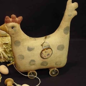 May include: A vintage pull-along toy chicken with grey polka dots, a red comb, and a decorative tag. The chicken has wheels and is connected to a wooden spool by a white string. Eggs and hay are in the background.