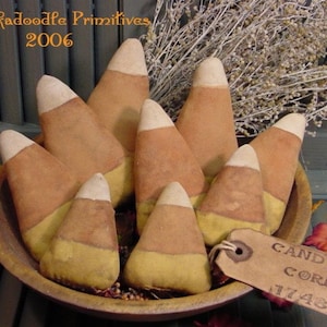 Könnte beinhalten: Eine Schüssel gefüllt mit handgemachtem Stoff-Candy Corn, einer beliebten Herbstdekoration. Die Schüssel ist aus Holz und hat eine rustikale Oberfläche. Das Candy Corn ist aus Stoff und hat ein realistisches Aussehen. Die Schüssel steht auf einer Holzoberfläche. Das Bild enthält auch ein Etikett mit der Aufschrift "Candy Corn 1748".
