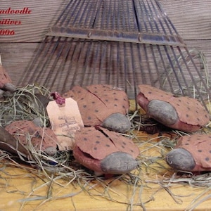 May include: Five brown and black ladybug-shaped fabric ornaments with black polka dots. The ornaments are sitting on a bed of straw with a rusty rake in the background. A tag with the text "Handmade with Love" is visible in the image.