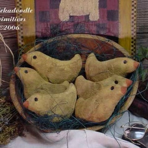 May include: A wooden bowl filled with a nest of straw and five small, hand-painted, yellow chicks. The chicks have black eyes and orange beaks. The bowl is sitting on a wooden surface.
