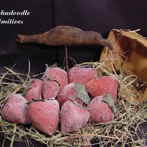 Può includere: Una collezione di fragole di feltro fatte a mano in un cesto con una statuetta di uccello in legno rustico. Le fragole sono di un rosso intenso e hanno una finitura bianca glassata. L'uccello è marrone e ha un becco lungo e sottile.