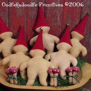 May include: Handmade gnome dolls with red hats and beige bodies, displayed in a wooden bowl with decorative mushrooms. The dolls are set against a rustic red background. The text "Oodlekadoodle Primitives ©2006" is visible.