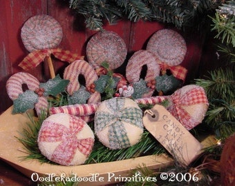 Puede incluir: Una colección de adornos navideños hechos a mano, que incluyen bastones de caramelo, piruletas y adornos redondos. Los adornos de tela tienen patrones de cuadros rojos y blancos y están espolvoreados con purpurina. Una etiqueta dice "Candy Cane Lane".