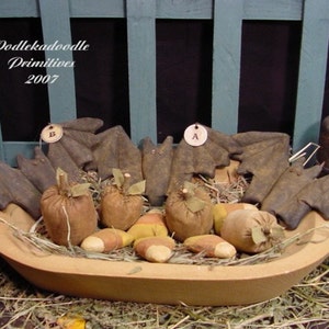 May include: A wooden bowl filled with handmade fabric bats, pumpkins, and candy corn. The bats have tags with the letters A, B, and TJ. The bowl is sitting on a bed of straw. The text "Oodleka doodle Primitives 2007" is visible in the top left corner of the image.