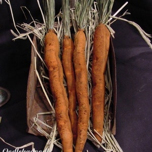 May include: Four orange fabric carrots with green tops are arranged in a metal container filled with straw. The carrots are handmade and have a rustic, vintage look.