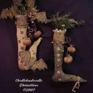 May include: Two handmade Halloween stockings with bat wings, pumpkins, and bells. The stockings are made of fabric and have a rustic, vintage look. The text "Oodleka doodle Primitives @2007" is visible at the bottom of the image.