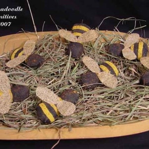May include: A bowl filled with hay and nine handmade felt bumblebees. The bees are black and yellow with brown wings. The bowl is made of wood and has a light brown finish.