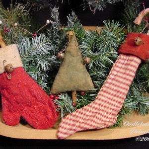 May include: Three handmade Christmas stockings with candy canes and bells. The stockings are red and white with a striped pattern. The stockings are sitting in a wooden bowl with green pine branches.