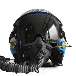 Könnte beinhalten: Blau-weißer Pilotenhelm mit dunklem Visier und grauer Sauerstoffmaske. Der Helm hat ein reflektierendes Visier und einen gewendelten grauen Schlauch. Auf dem Helm steht das Wort "COMMANDER".