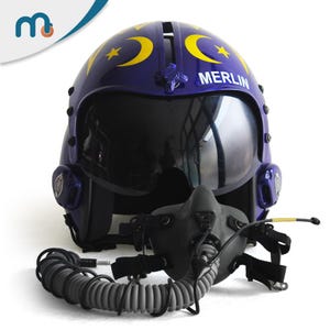 Könnte beinhalten: Blauer Pilotenhelm mit Visier, verziert mit gelben Monden und Sternen. Das Wort "MERLIN" ist auf der Vorderseite aufgedruckt. Er hat eine dunkelgraue Sauerstoffmaske und einen gewickelten grauen Schlauch.