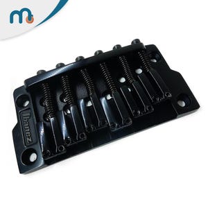 Puede incluir: Un puente de guitarra Ibanez negro con seis selletas y muelles ajustables. El puente es de metal y tiene un diseño elegante. El logotipo de Ibanez es visible. Esta pieza de guitarra está diseñada para guitarras eléctricas.