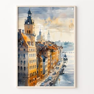 May include: Watercolor painting of a cityscape with a tall clock tower and other buildings along a waterfront. The buildings are painted in shades of yellow, orange, and brown. A boat is docked in the water.