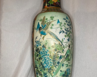 May include: A tall, decorative ceramic vase with a detailed floral and bird design. The vase features a light green background with blue and green birds, flowers, and foliage. The top and base have gold accents, and the neck has a black background with colorful flowers.