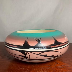 Könnte beinhalten: Handbemalte Keramikschale mit südwestlichem Design. Die Schale hat einen türkisfarbenen Innenraum, einen rosa-orangenen Farbverlauf und schwarz-weiße geometrische Muster mit stilisierten Bäumen und Bergen.