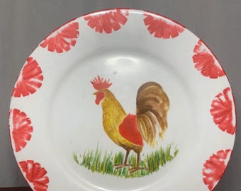 May include: White plate with a hand-painted rooster design. The rooster is yellow, red, and brown, standing on green grass. The rim of the plate is decorated with red floral patterns.