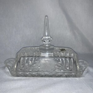 May include: A clear glass butter dish with a lid and a decorative knob on top. The dish has a diamond pattern.