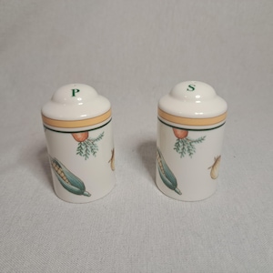 Pode incluir: Um conjunto de dois saleiros e pimenteiros de cerâmica branca com um design de vegetais verde, amarelo e laranja. Os saleiros são etiquetados com "S" e "P".