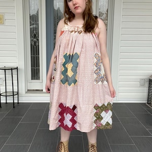 Könnte beinhalten: Ein hellrosa Patchwork-Kleid mit verschiedenen bunten geometrischen Mustern. Das Kleid hat einen quadratischen Ausschnitt und eine lockere, fließende Silhouette. Das Model trägt beige Schnürstiefel.