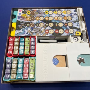 May include: A white organizer insert for the board game "The Crew: The Quest for Planet Nine". The insert has compartments for the game's cards, dice, and tokens. The insert is labeled "Parent Foxes".