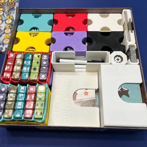 May include: A white box with dividers for organizing game components. The box contains a variety of colored dice, cards, and tokens. The box is labeled "Adventure Cards" and "Story Cards".