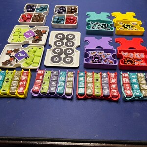 May include: A set of colorful plastic trays with compartments for storing small game pieces. The trays are arranged in rows on a blue surface. The trays are labeled with numbers, including "1st", "2nd", and "3rd".