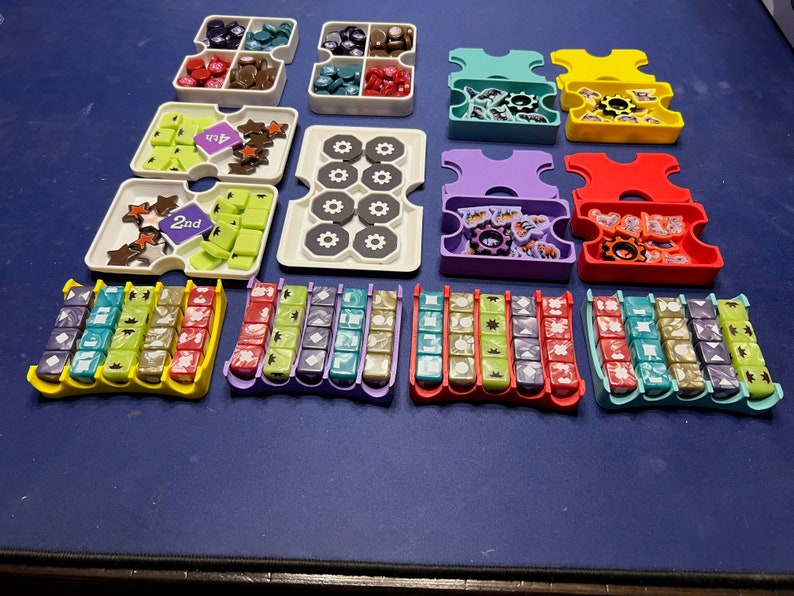 May include: A set of colorful plastic trays with compartments for storing small game pieces. The trays are arranged in rows on a blue surface. The trays are labeled with numbers, including "1st", "2nd", and "3rd".