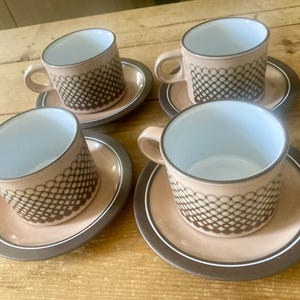 May include: Four matching coffee cups and saucers. The cups and saucers are a light peach colour with a dark brown geometric pattern on the cups. The saucers have a dark brown rim. The cups have a light blue interior.