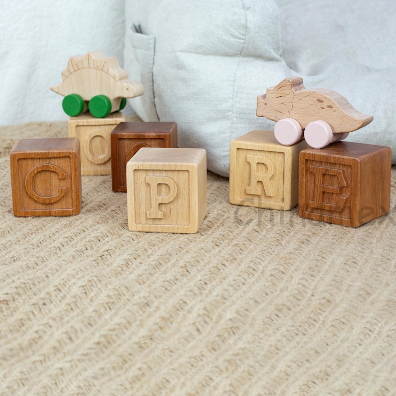 May include: Wooden blocks spelling out the word "CORE" with a green and brown dinosaur toy on top of the "C" block and a pink and brown dinosaur toy on top of the "R" block.