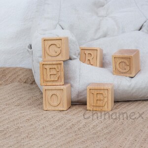 May include: Wooden blocks spelling out the word "GEORGE" in all caps. The blocks are stacked on top of each other and are sitting on a brown hessian surface.