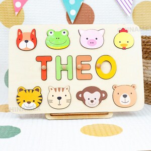 May include: Wooden puzzle board with colorful animal and letter pieces. The board has the name "THEO" spelled out with colorful letters and features animal faces including a frog, pig, chicken, tiger, cat, monkey, and bear.
