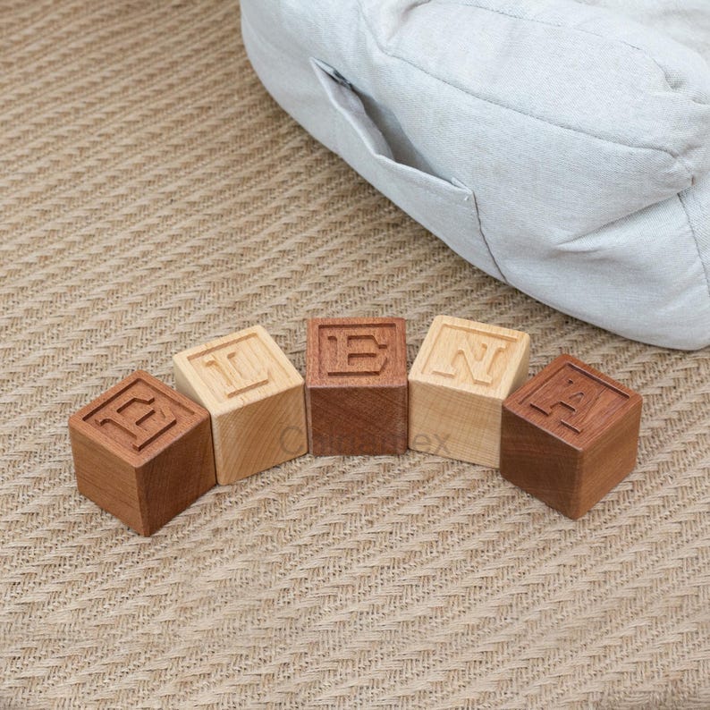 May include: Five wooden blocks spelling out the word "BEAN" in all caps. The blocks are arranged in a semi-circle on a light brown surface.