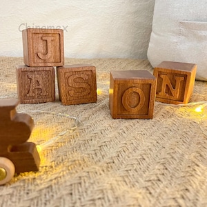May include: Four wooden blocks spelling out the name "Jason" in all-caps. The blocks are a light brown colour and have a smooth, polished finish.