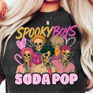 Puede incluir: Camiseta negra con un gráfico de cinco figuras de esqueletos con varios peinados y ropa. Las palabras "SPOOKY BOYS" y "SODAPOP" están en rosa y amarillo, con corazones rosas. El diseño tiene una estética retro y vintage.