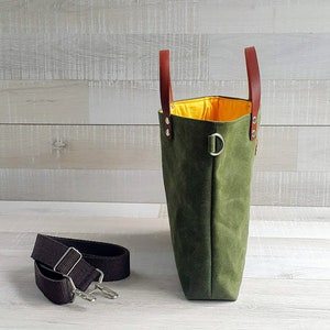 May include: A green canvas tote bag with brown leather handles and a yellow lining. The bag has a detachable shoulder strap.