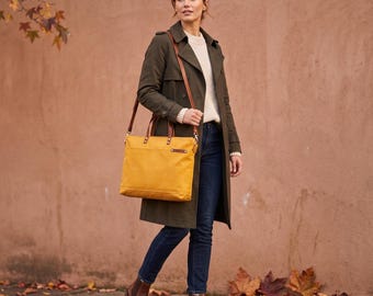 May include: A mustard yellow rectangular tote bag with brown leather handles and a detachable shoulder strap. The bag features a horizontal front pocket with a small brown leather accent tab, silver-toned hardware, and a structured design.