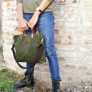 May include: A green canvas tote bag with brown leather handles and a brown adjustable shoulder strap. The bag has a yellow lining and a brown leather patch on the front.