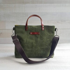 May include: A green canvas tote bag with brown leather handles and a brown adjustable shoulder strap. The bag has a zipper closure and a small pocket on the front.