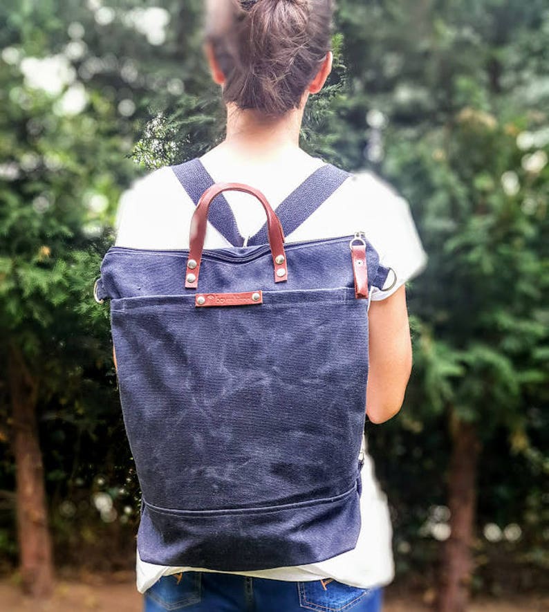 May include: A dark blue canvas backpack with brown leather straps and handles. The backpack has a zipper closure and a flap with a metal buckle.