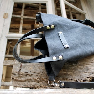 Op de afbeelding: Een zwarte canvas tote bag met leren banden en een zilveren gesp. De tas heeft een klein leren patch met het woord "REBEL" erop.