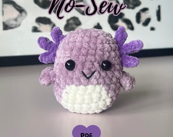 May include: A plush, lavender axolotl with purple gills and black eyes. The axolotl has a white belly and a smiling face. The words "No-Sew" are written above the axolotl, and a purple heart with "PDF" is below.