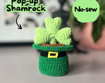 May include: A green crocheted shamrock pops up from a green crocheted pot shaped like a leprechaun's hat. The hat has a black band with a gold buckle. The text "No-sew" is written on a green circle.