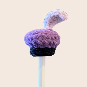 May include: Purple and black crocheted cupcake pencil topper with a white fluffy swirl on top.