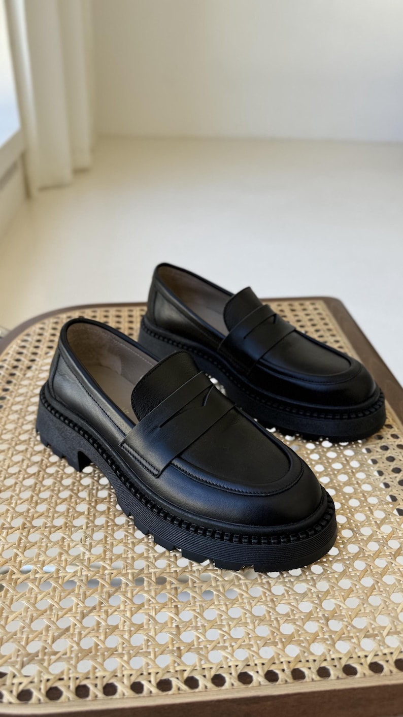 Puede incluir: Dos pares de mocasines de cuero negro con suela de plataforma gruesa. Los mocasines tienen un dise&ntilde;o sencillo con una sola correa en la parte superior.