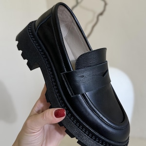 Puede incluir: Zapatos de vestir negros de cuero con suela de plataforma gruesa y un detalle de costura decorativa alrededor del borde.