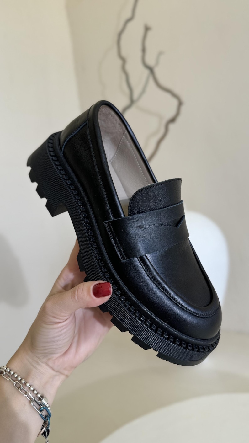 Puede incluir: Zapatos de vestir negros de cuero con suela de plataforma gruesa y un detalle de costura decorativa alrededor del borde.