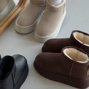 May include: Three pairs of ankle boots with thick platform soles and plush interior lining. One pair is beige suede, one is dark brown suede, and one is black leather-textured material. Each boot features a rounded toe and a pull tab.