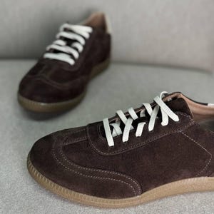 May include: A pair of brown suede trainers with white laces. The trainers have a brown rubber sole.