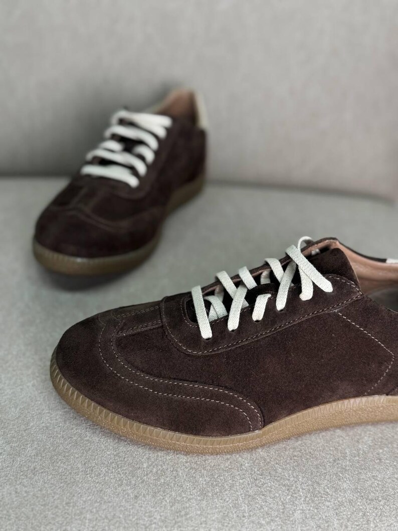 May include: A pair of brown suede trainers with white laces. The trainers have a brown rubber sole.